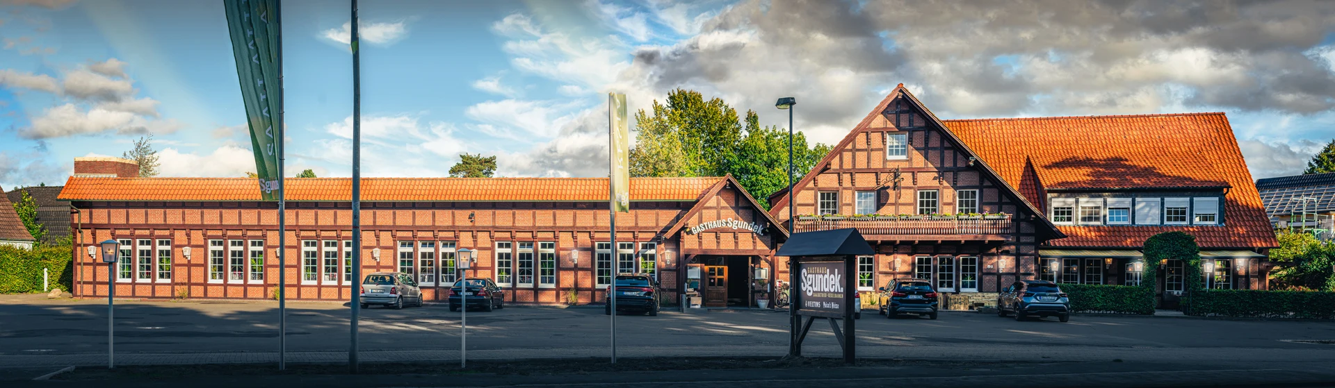 Außenansicht Gasthaus Sgundek - Das typische Fachwerkhaus für die Region Vechta mit dem großen Saal links, dem Haupteingang in der Mitte und dem Restaurant mit Biergarten und Terrasse auf der rechten Seite. Oben, über dem Restaurant liegen die gemütlichen Hotelzimmer, zwei davon mit Balkonzugang. Der große Platz vor dem Gebäude bietet viel Raum zum freien Parken.